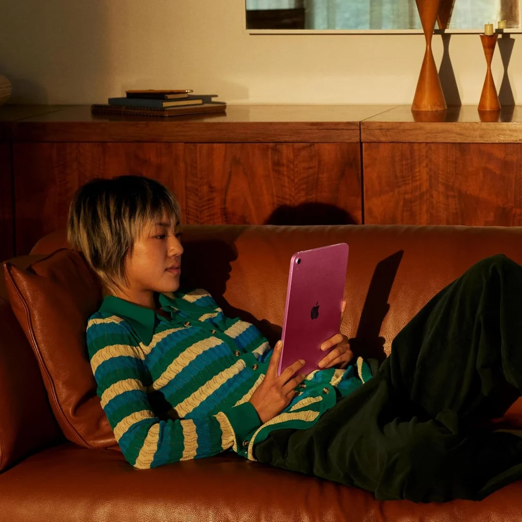 Person relaxing on leather couch using pink iPad tablet at home