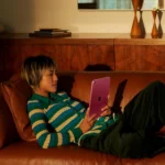 Person relaxing on leather couch using pink iPad tablet at home