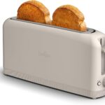 Slim beige Bella 2 Slice Slim Toaster with extra-long slot holding two slices of toasted bread, featuring shade control dial, cancel button, and compact fits-anywhere kitchen design.