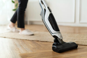 Person vacuuming a wooden floor with a cordless stick vacuum cleaner.
