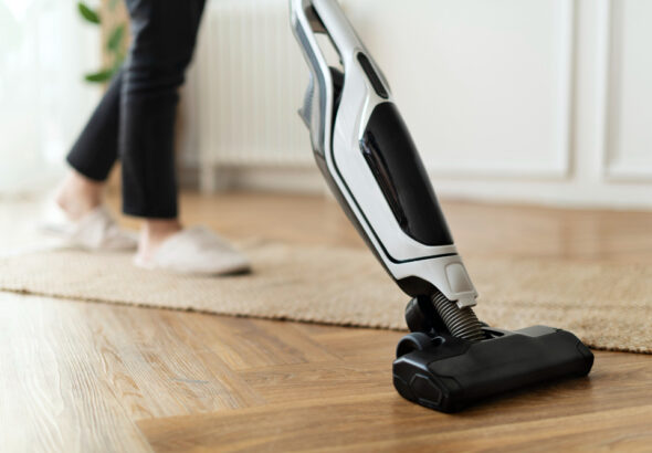 Person vacuuming a wooden floor with a cordless stick vacuum cleaner.