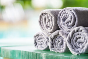 Soft gray bath towels neatly rolled and stacked on a wooden surface with a blurred spa-like background, creating a clean and relaxing atmosphere.