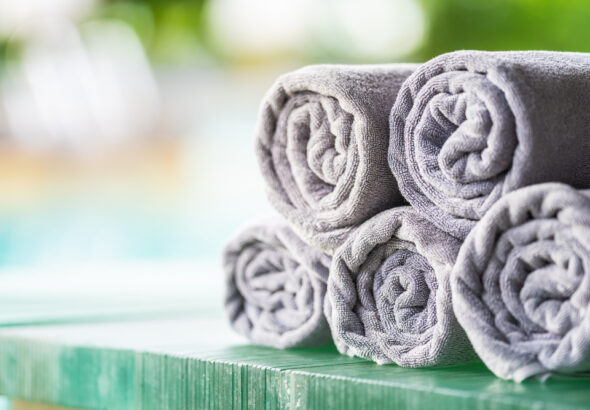 Soft gray bath towels neatly rolled and stacked on a wooden surface with a blurred spa-like background, creating a clean and relaxing atmosphere.
