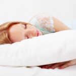 Young woman sleeping peacefully on a white pillow in a bright, comfortable bedroom.