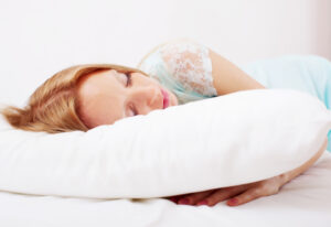 Young woman sleeping peacefully on a white pillow in a bright, comfortable bedroom.