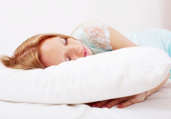 Young woman sleeping peacefully on a white pillow in a bright, comfortable bedroom.