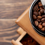 Coffee grinder with fresh whole beans and ground coffee on a kitchen counter