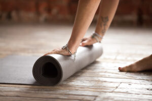 Rolled yoga mat and folded travel mat on a wood floor